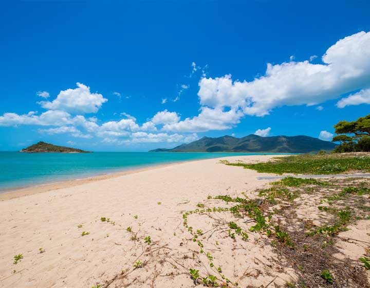 Empty sandy beach at Cape Gloucester with Gloucester Island and a mountain range across the turquoise water
