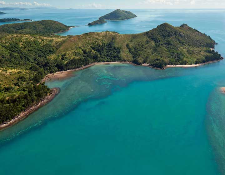Aerial view of forested Whitsunday islands, fringing reef and turquoise water from a helicopter flight out of Airlie Beach