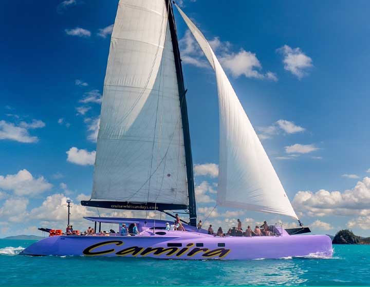 Camira, a purple Cruise Whitsundays sailing catamaran, under full sail with guests on deck in the Whitsunday Islands
