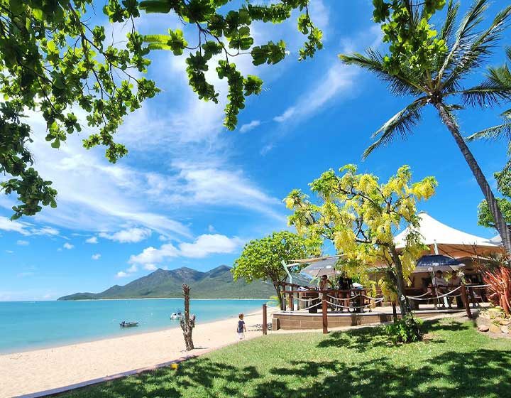 Beachfront deck and palms at Cape Gloucester, with the sand, turquoise water and Gloucester Island behind