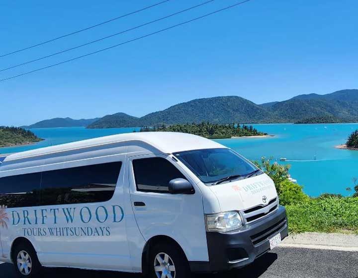 Driftwood Tours Whitsundays van parked at a lookout above Shute Harbour, with turquoise water and the Whitsunday islands behind