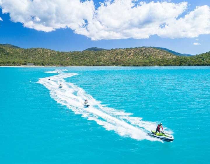 Line of jet skis carving a wake across a turquoise bay in the Whitsunday Islands