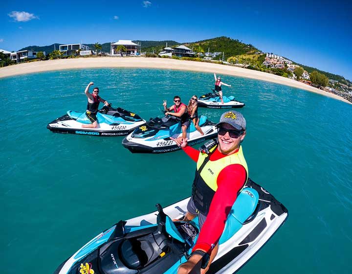Guide and guests on jet skis waving on the water off an Airlie Beach bay