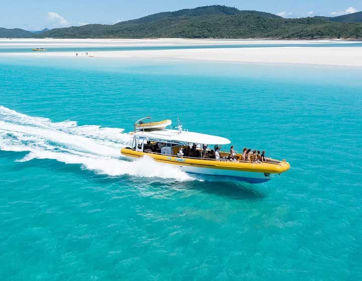Yellow speed boat with guests on board crossing the turquoise water off Hill Inlet and Whitehaven Beach
