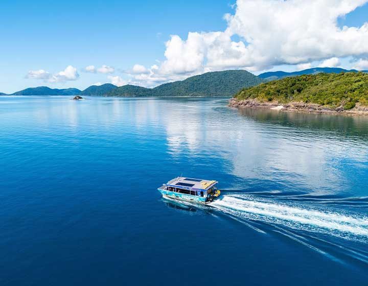 Pioneer Adventures glass bottom boat cruising calm blue water among the forested islands near Shute Harbour