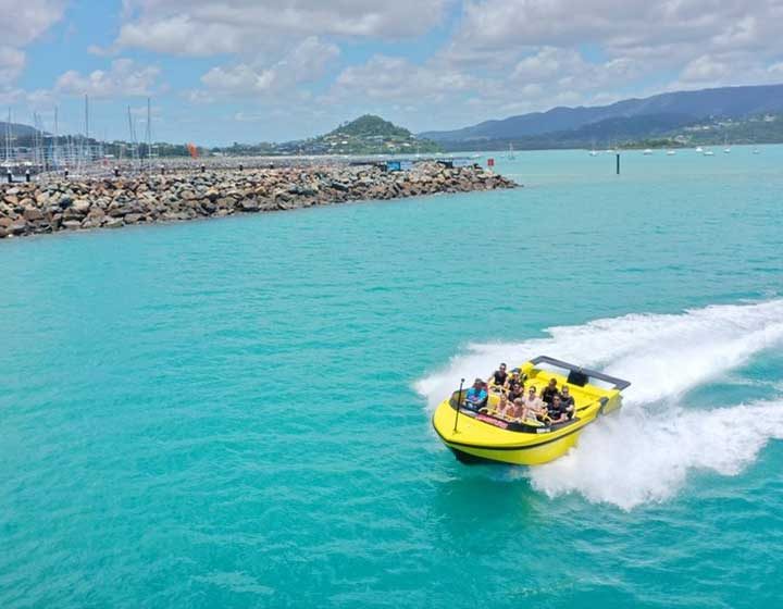Yellow Pioneer Adventures jet boat full of guests turning hard beside the Coral Sea Marina breakwall, Airlie Beach