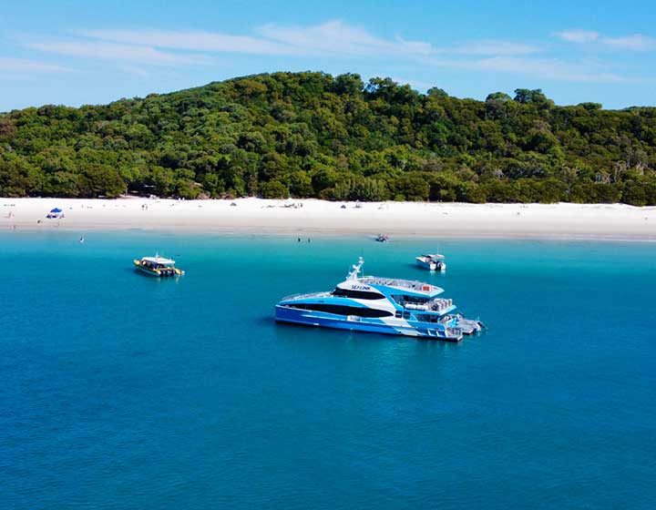 SeaLink catamaran anchored off Whitehaven Beach on Whitsunday Island, with the white sand and forest behind