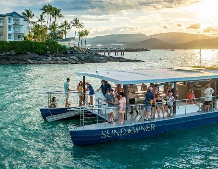 Guests on board the Sundowner sunset cruise boat on Pioneer Bay, with Airlie Beach and the hills behind in the late afternoon light