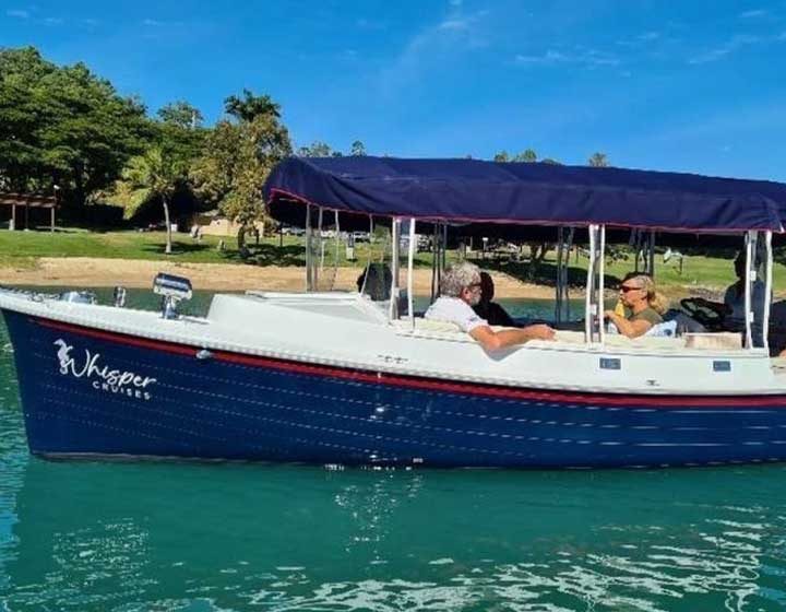 Guests on a navy blue Whisper Cruises electric boat on the water off the Airlie Beach foreshore