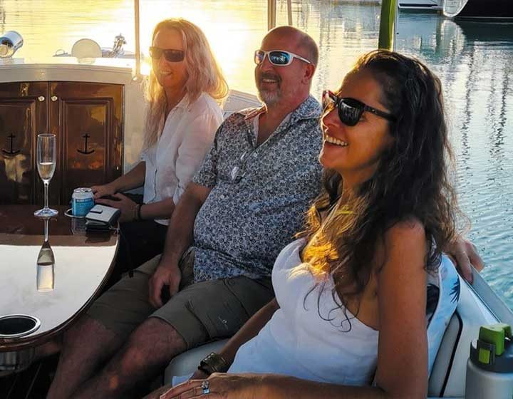 Three guests with a glass of bubbles on a Whisper Cruises electric boat at golden hour in Coral Sea Marina
