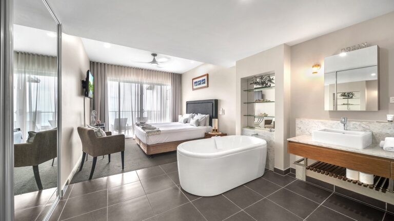 Freestanding bath, marble vanity and king bed in the open-plan main bedroom with terrace beyond, 1 bedroom apartment at Whitsunday Reflections, Airlie Beach
