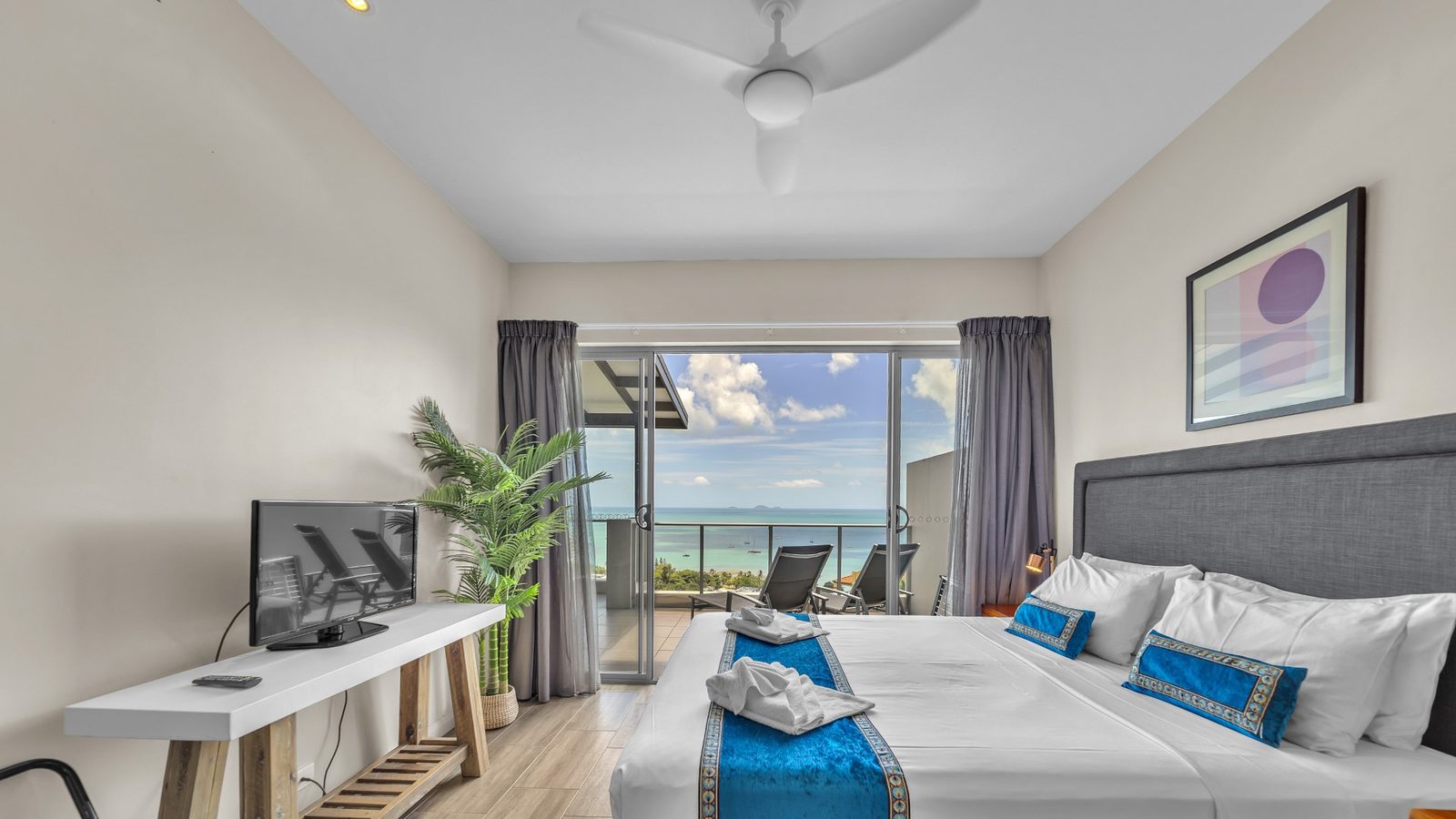 King bed facing sliding doors to the terrace, sun lounges and the Coral Sea, 1 bedroom apartment at Whitsunday Reflections, Airlie Beach