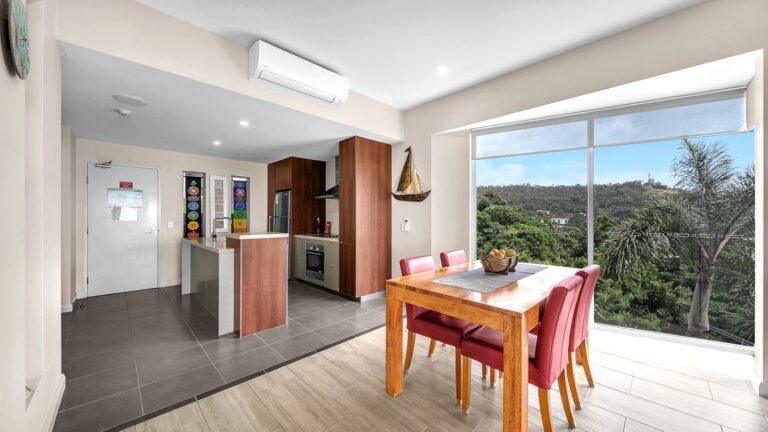Kitchen with island bench and Bosch oven, timber dining table and floor-to-ceiling windows over the hillside above Airlie Beach, 1 bedroom apartment at Whitsunday Reflections