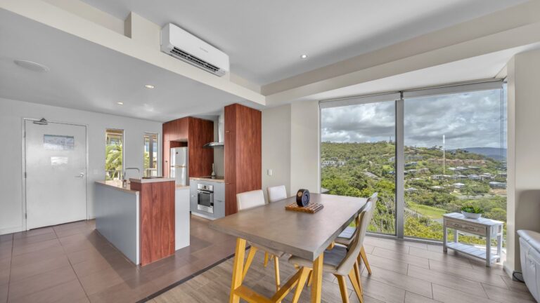 Kitchen with island bench, Bosch oven and full-size fridge beside a dining table for four with hillside views, 1 bedroom apartment at Whitsunday Reflections, Airlie Beach