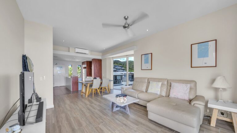 Open-plan living with leather lounge, dining table, kitchen and view to the hillside, 1 bedroom apartment at Whitsunday Reflections, Airlie Beach