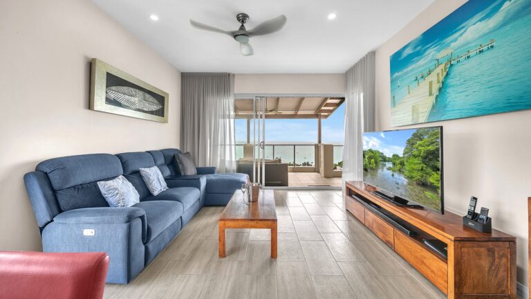Lounge with blue sofa, Smart TV and sheer curtains opening to a covered balcony over Pioneer Bay, 1 bedroom apartment at Whitsunday Reflections, Airlie Beach