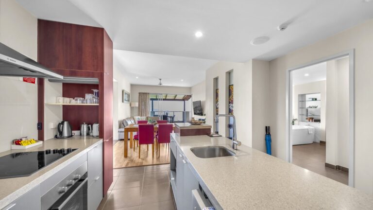 Galley kitchen with Bosch rangehood and stone benches opening to the lounge, dining and balcony, 1 bedroom Garden View apartment at Whitsunday Reflections, Airlie Beach