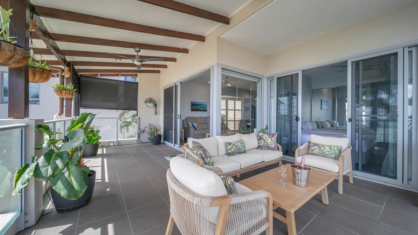 Covered balcony with outdoor lounge, coffee table and champagne, with sliding doors to the living room and main bedroom, 2 bedroom apartment at Whitsunday Reflections, Airlie Beach