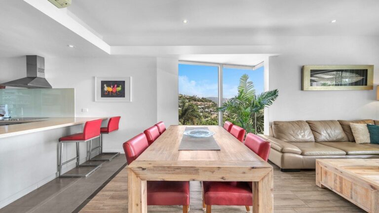Dining table for six and kitchen breakfast bar with stools beside a corner window over the hills behind Airlie Beach, 2 bedroom apartment at Whitsunday Reflections