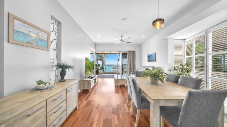 Dining table for six, lounge and Smart TV looking through open doors to the balcony and the ocean, 2 bedroom apartment at Whitsunday Reflections, Airlie Beach