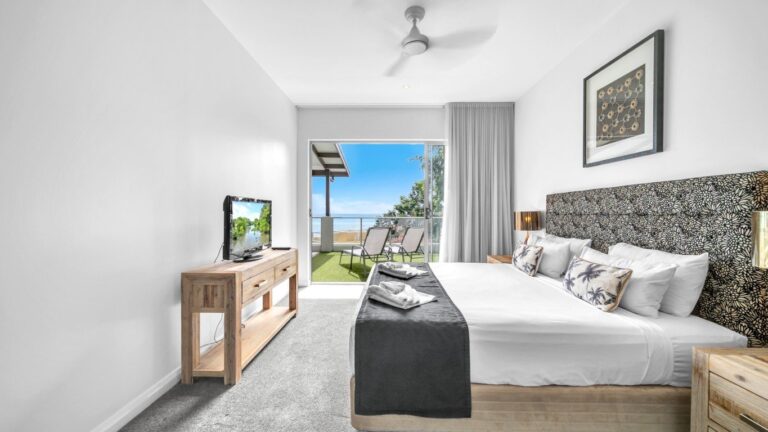 King bed facing sliding doors to a courtyard with sun lounges and an ocean view, 2 bedroom apartment at Whitsunday Reflections, Airlie Beach