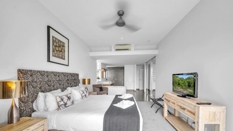King bed with patterned headboard and ceiling fan, looking through to a freestanding bath and ensuite, 2 bedroom apartment at Whitsunday Reflections, Airlie Beach
