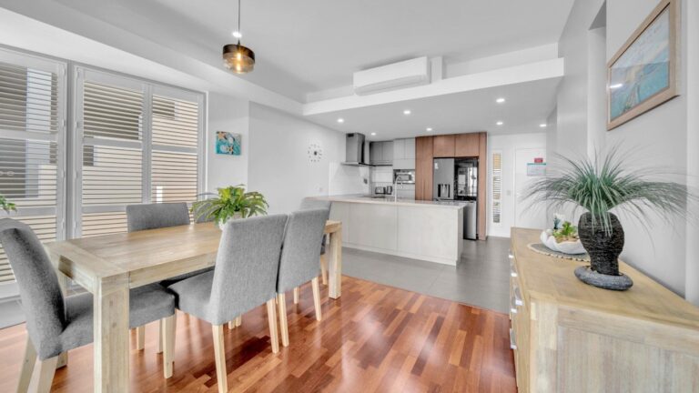 Kitchen with stone island bench, full-size fridge and rangehood beside a dining table for six, 2 bedroom apartment at Whitsunday Reflections, Airlie Beach