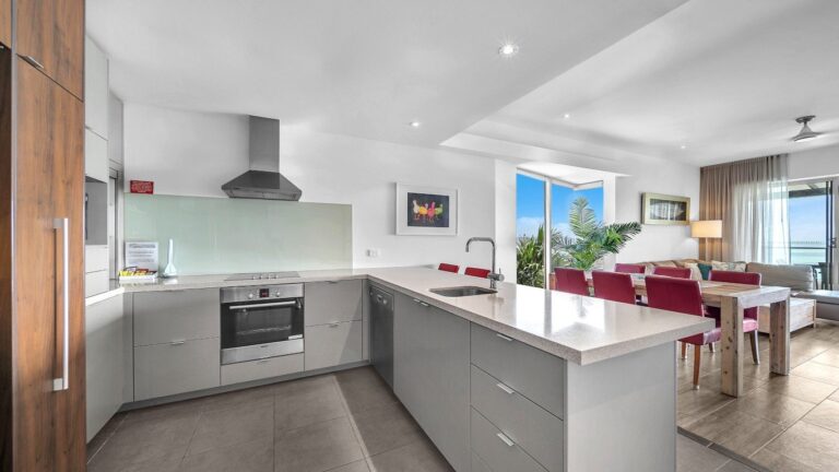Kitchen with stone benches, Bosch oven, dishwasher and full-size fridge looking through the dining and lounge to the balcony and ocean, 2 bedroom apartment at Whitsunday Reflections, Airlie Beach