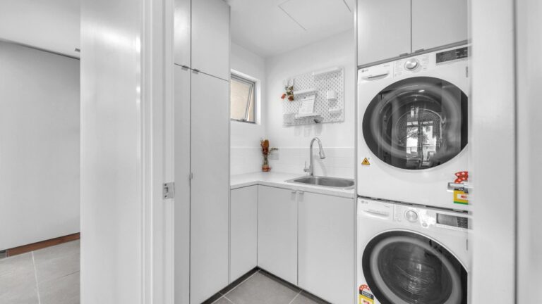 Laundry with stacked washing machine and dryer, laundry sink and storage cupboards, 2 bedroom apartment at Whitsunday Reflections, Airlie Beach