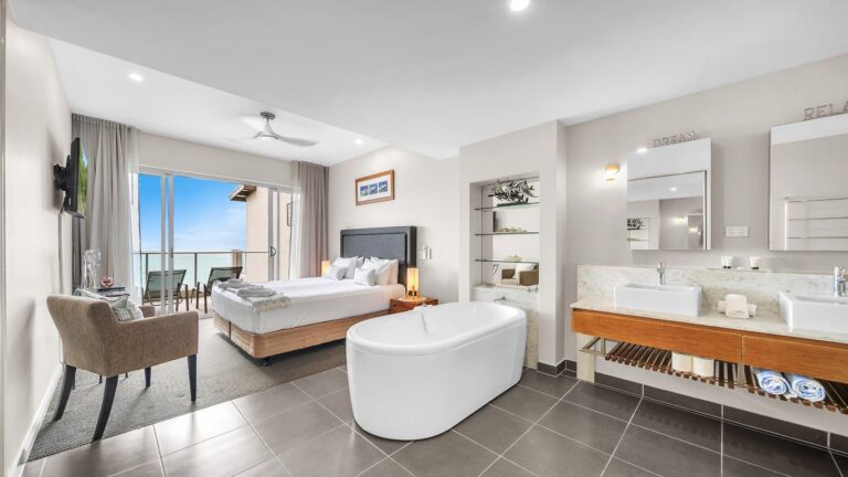 King bed, freestanding bath and twin basins in an open-plan main bedroom with sliding doors to a balcony over the ocean, 2 bedroom apartment at Whitsunday Reflections, Airlie Beach