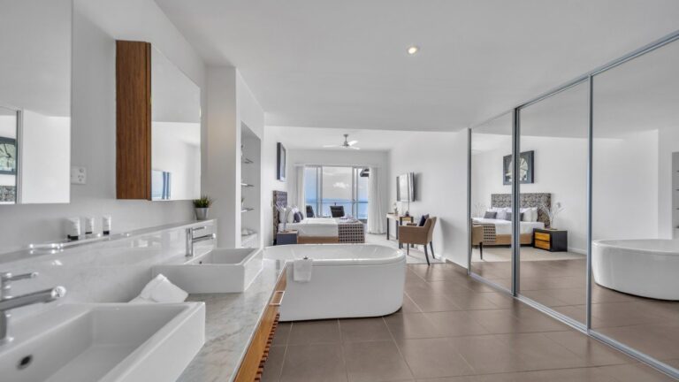 Freestanding bath and twin basins on a marble vanity in the open-plan main bedroom, with king bed, mirrored robe and ocean view, 2 bedroom Premium Ocean View apartment at Whitsunday Reflections, Airlie Beach