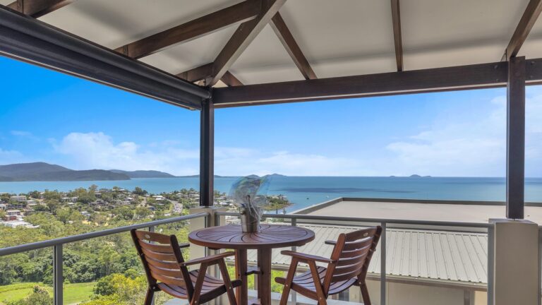 Timber bar table and two chairs on a covered balcony looking over Airlie Beach and Pioneer Bay to the Coral Sea, 3 bedroom apartment at Whitsunday Reflections
