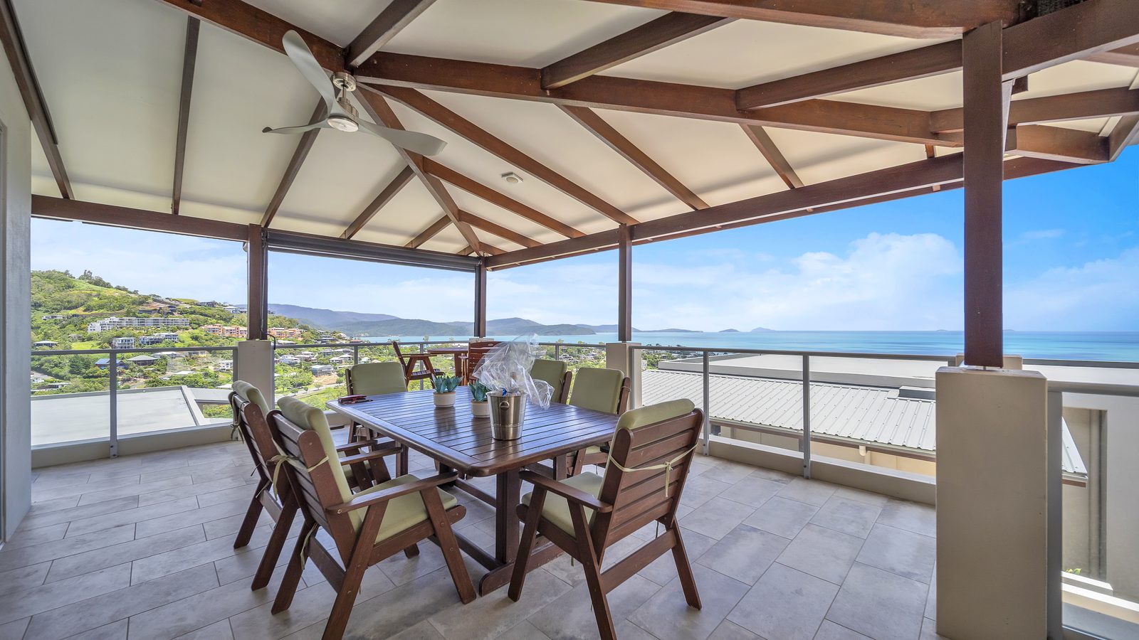 Covered balcony with a timber outdoor dining table for six and ceiling fan, looking over Airlie Beach and Pioneer Bay to the Coral Sea and Whitsunday Islands, 3 bedroom apartment at Whitsunday Reflections