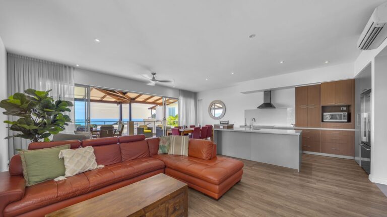 Leather corner lounge looking across the dining table and kitchen to the covered balcony and ocean, 3 bedroom apartment at Whitsunday Reflections, Airlie Beach