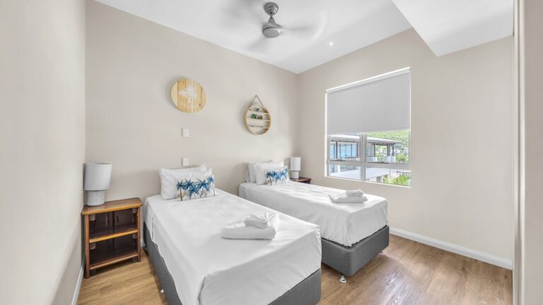 Third bedroom with two single beds, bedside tables and a ceiling fan, 3 bedroom apartment at Whitsunday Reflections, Airlie Beach