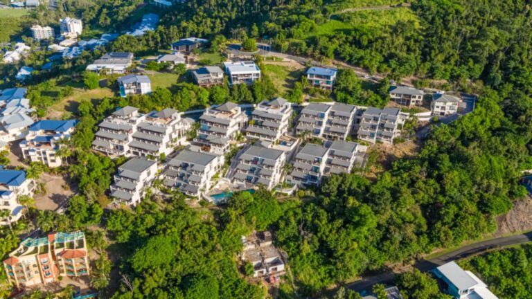 Overhead aerial of Whitsunday Reflections apartment buildings terraced down the hillside on Horizons Way, with the lap pool and heated spa among the gardens and rainforest, Airlie Beach