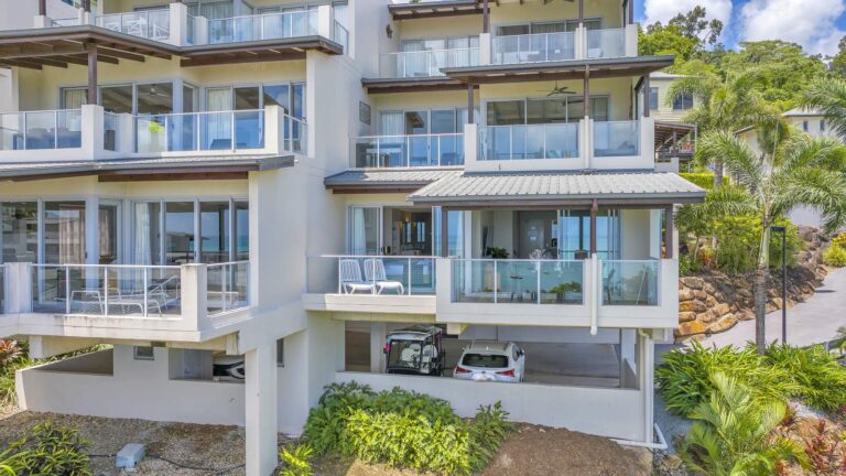 Apartment building with covered glass balconies over undercover parking, with tropical gardens and a glimpse of the Coral Sea through the windows, Whitsunday Reflections, Airlie Beach