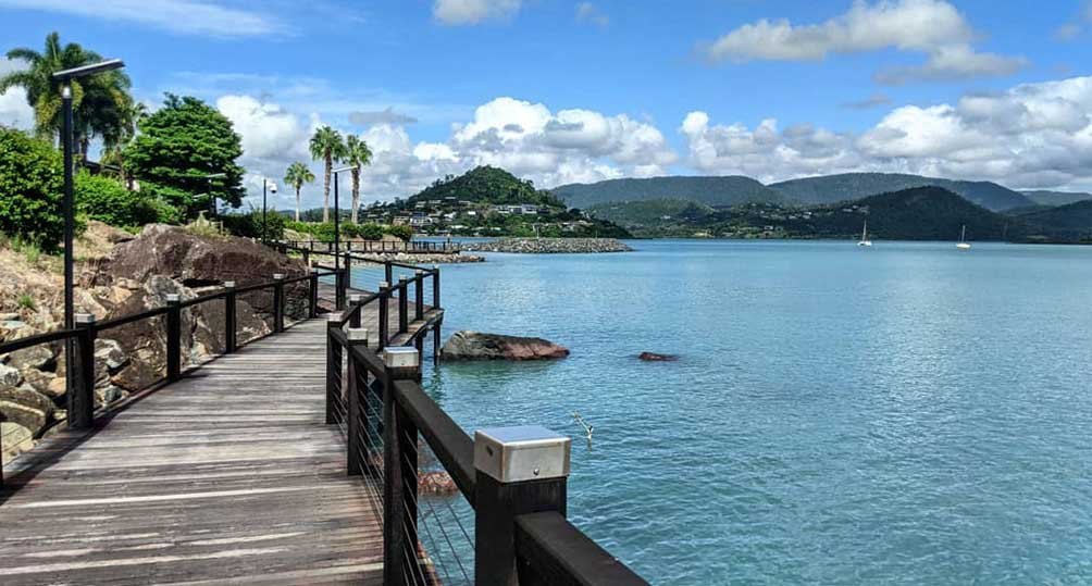The timber boardwalk of the Bicentennial Walkway running along the water at Airlie Beach, with yachts moored in the bay