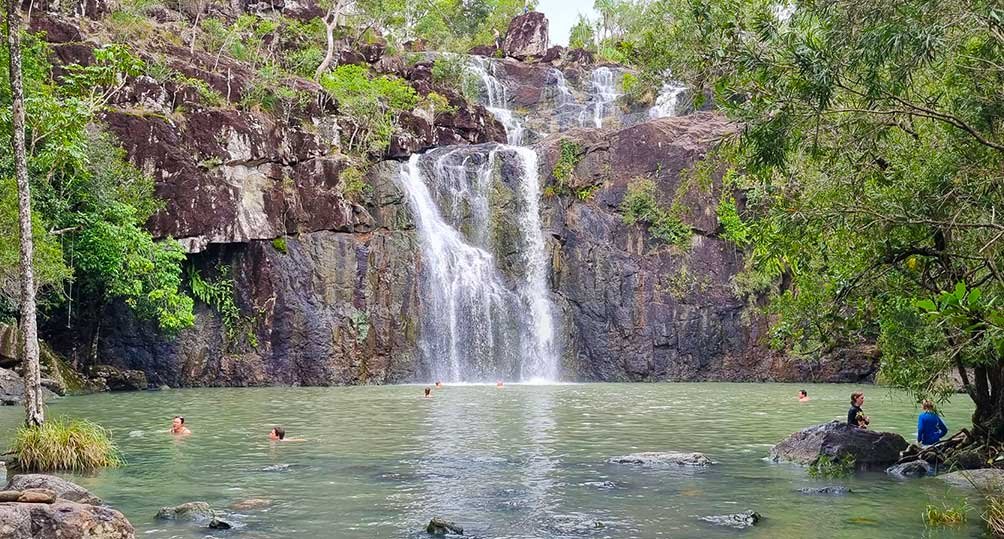 Cedar Creek Falls flowing into a fresh-water swimming hole, with swimmers in the water, Conway National Park