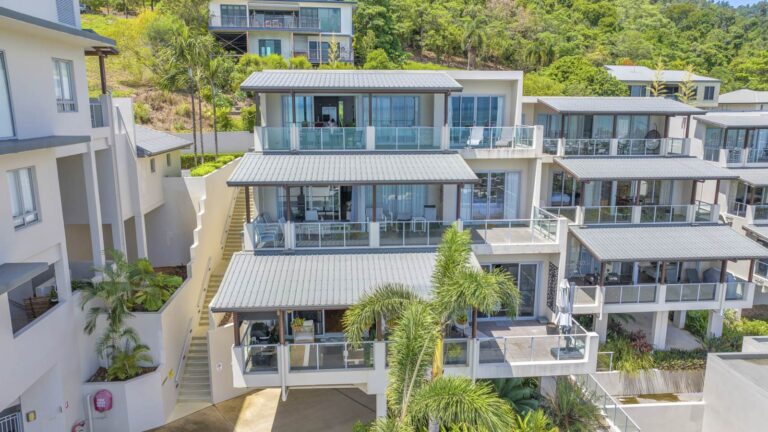 Three levels of covered apartment balconies with outdoor furniture, beside garden stairs and palms, Whitsunday Reflections, Airlie Beach