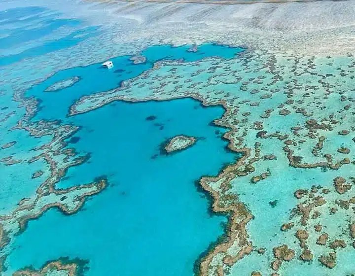 Aerial view of Hardy Reef on the outer Great Barrier Reef, with a boat moored in a deep blue lagoon surrounded by coral and the small heart-shaped Heart Reef in the centre