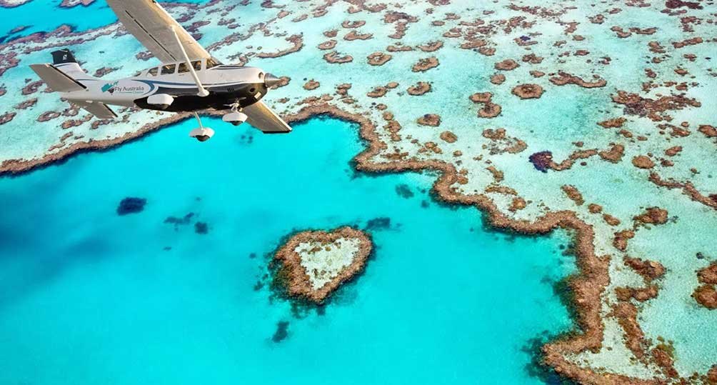 A light plane flying over Heart Reef, a small heart-shaped coral reef in turquoise water inside Hardy Reef, on the Great Barrier Reef