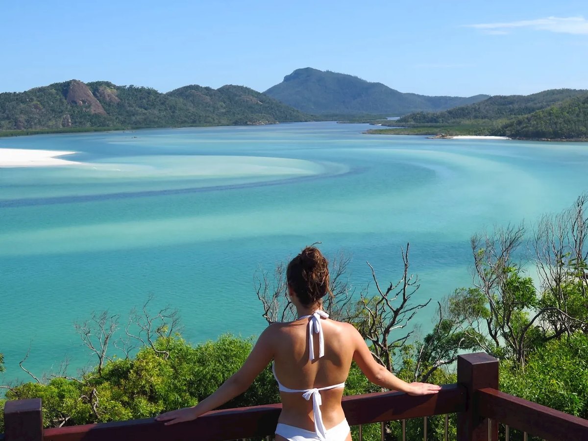 A visitor at a timber lookout rail above Hill Inlet on Whitsunday Island, with turquoise water, sand bars and forested hills beyond