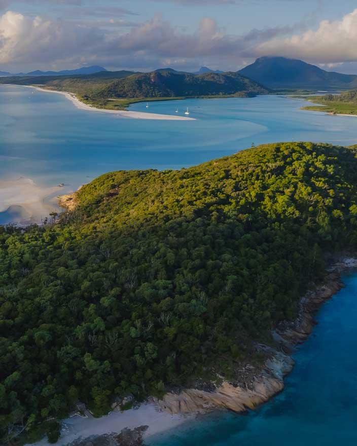 Aerial view over forested headland to Hill Inlet and the white silica sand of Whitsunday Island, one of the tours booked at the Whitsunday Reflections tour desk