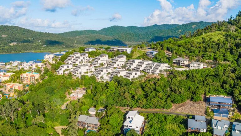 Aerial view of the white terraced apartment buildings of Whitsunday Reflections on the hillside above Airlie Beach, surrounded by rainforest with green hills behind