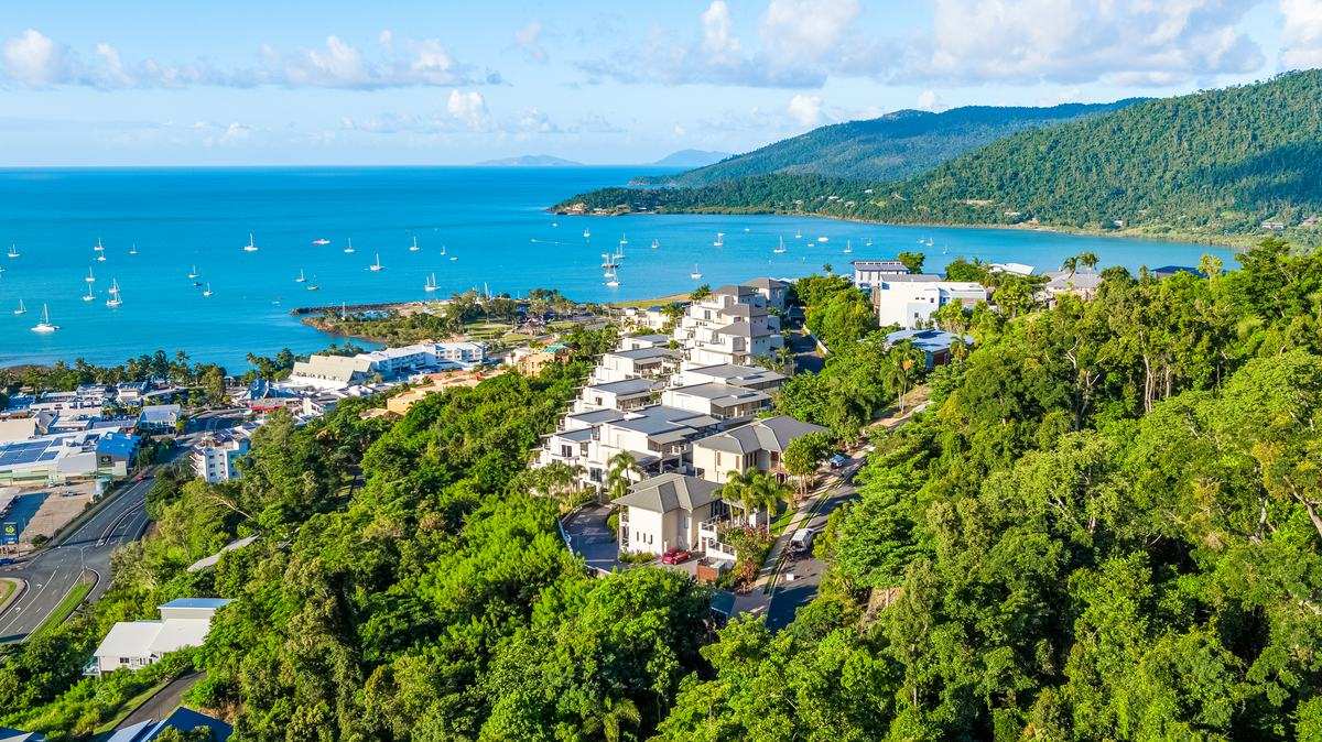 Aerial view of Whitsunday Reflections apartments on the hill above Airlie Beach with Pioneer Bay and the Coral Sea behind