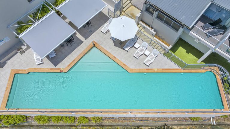 Overhead drone view of the 20 metre lap pool with its shallow end, sun lounges, umbrella and shaded seating on the pool deck, Whitsunday Reflections, Airlie Beach