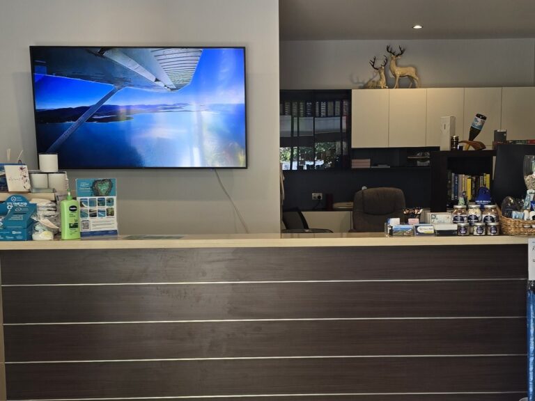 Whitsunday Reflections reception desk with tour brochures on the counter and a screen showing a scenic flight over the Whitsunday Islands, Airlie Beach