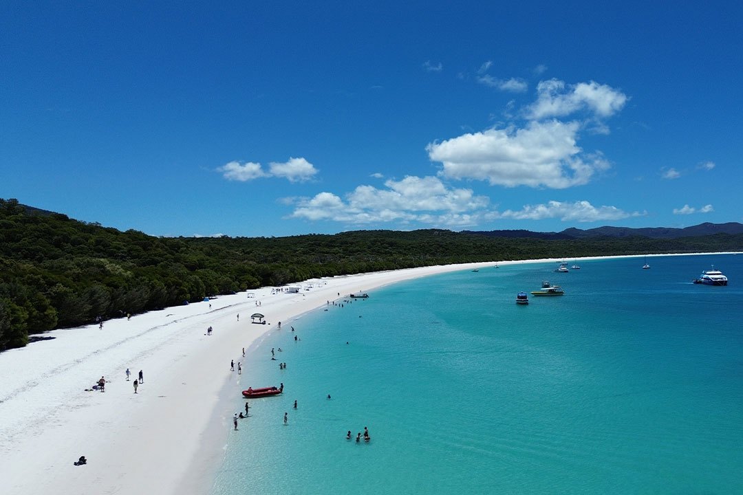 Swimmers in shallow turquoise water off Whitehaven Beach, with a red tender on the sand and boats anchored offshore, Whitsunday Island