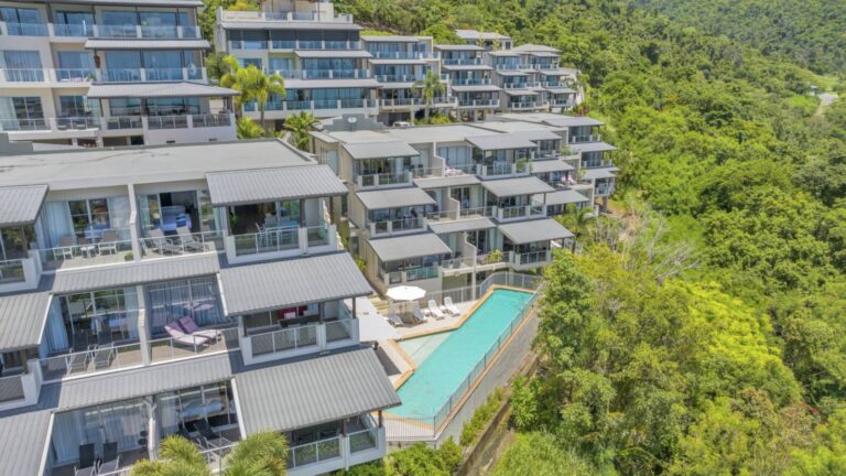 Aerial view of Whitsunday Reflections apartment buildings with covered balconies stepping down the hillside to the lap pool on the edge of the rainforest, Airlie Beach